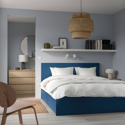 Blue MALM bed, white linens, light blue walls. Chair left, pendant light, shelf with lamp & decor.
