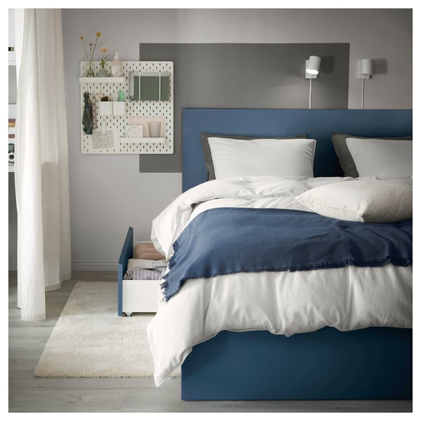 Modern bedroom with blue MALM bed, white linens, and pegboard wall decor.