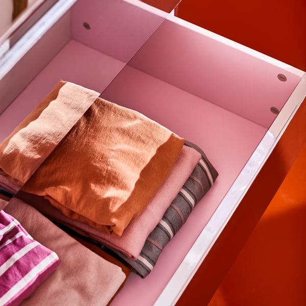 Pink drawers with reflective surface, showing organised storage of folded clothes. Safety fitting included.
