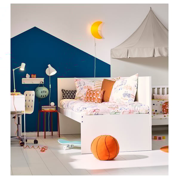 Childs bedroom with white bed, colourful pillows, orange stool, blue wall, and moon lamp.
