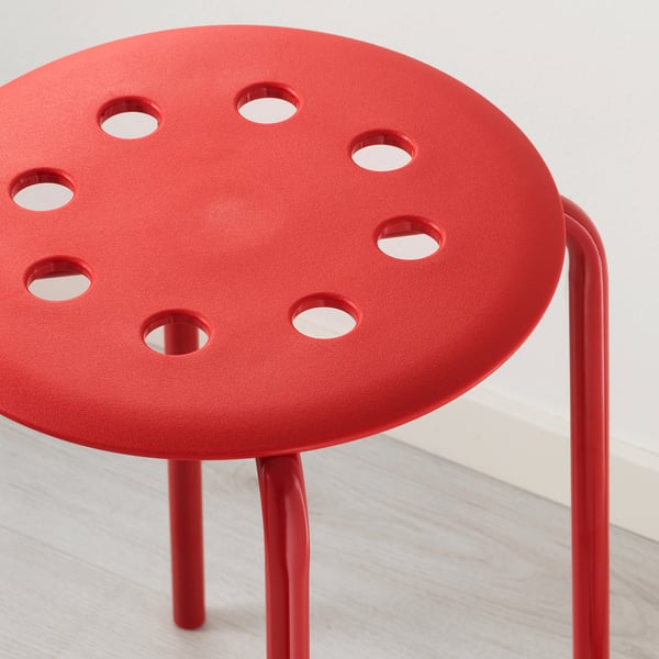 Bright red modern stool with circular holes in seat, sturdy metal legs, minimalist design.