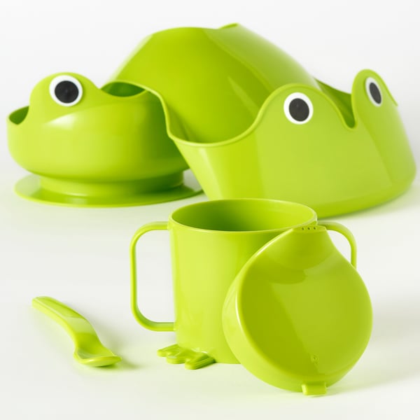 Bright green kids mealtime set: frog-shaped bowl, cup with handles, spoon, and adjustable bib, designed for independent eating and drinking.