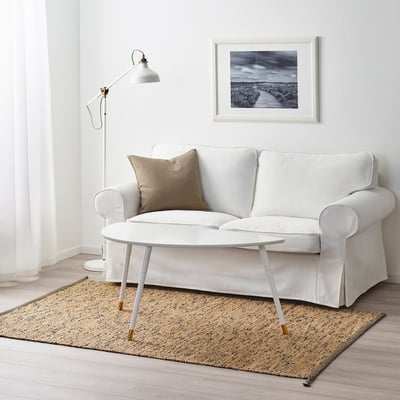 Minimalist living room: white MELHOLT jute rug, small white sofa, coffee table, beige pillow, floor lamp, framed art.