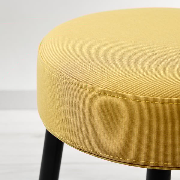 Close-up of a modern, round, yellow upholstered stool with sleek black legs, showcasing its quality fabric and clean design.