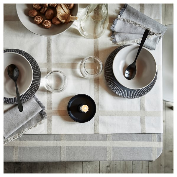 Elegant NISSÖGA beige tablecloth with subtle pattern, made of cotton and jute, set with plates, glasses, and cutlery.