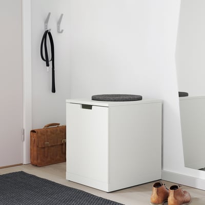 Modern white NORDLI chest with grey cushion, next to entrance with welcome mat, bag, and shoe rack.