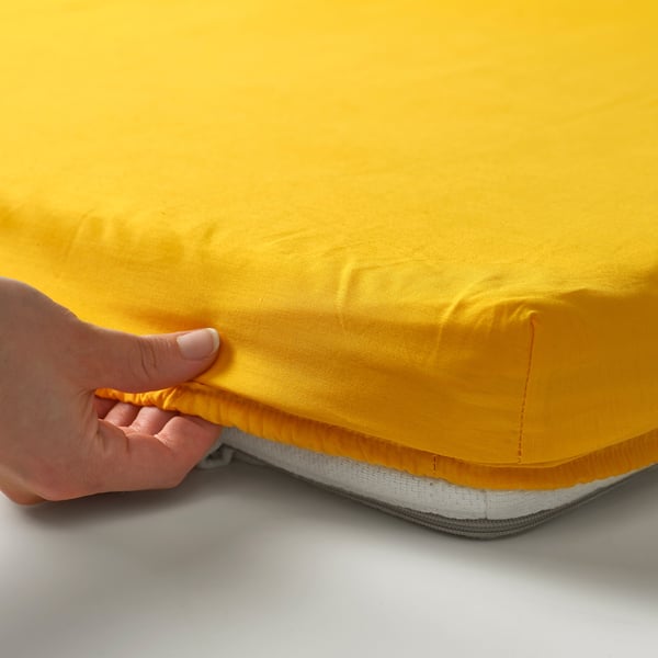 A hand zips a yellow fitted sheet on a mattress.