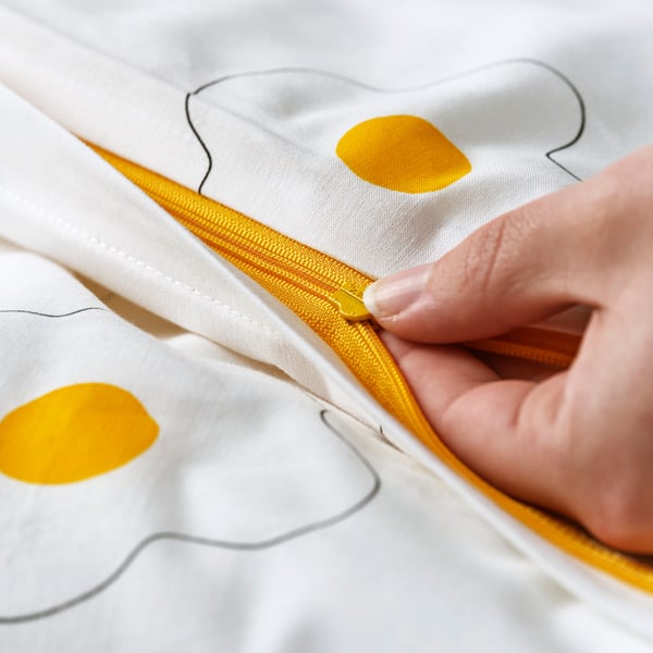 A hand pulls a yellow zip on white bedlinen with yellow spots, highlighting its safe design for children.