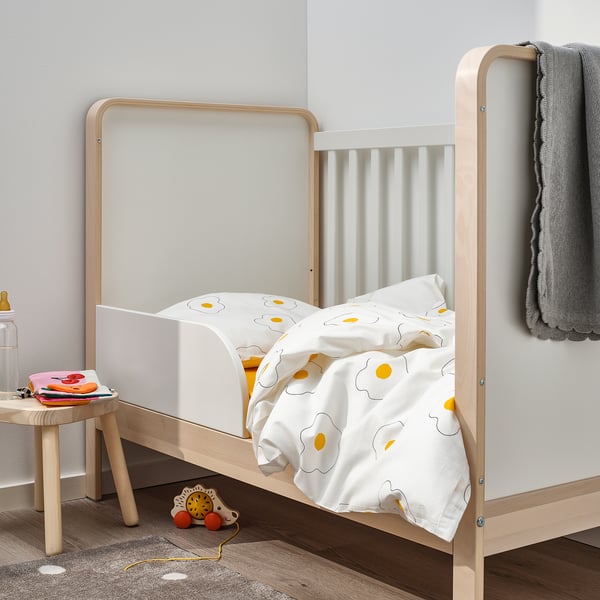 A cosy white wooden toddler bed with a sunflower-patterned blanket, small and fitting in a childs room.