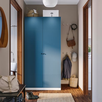 Modern entryway with tall blue PAX wardrobe, hooks, mirror, and rug.