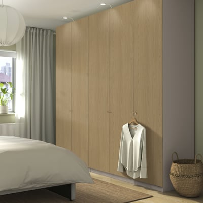Modern bedroom with wooden PAX wardrobe, wicker basket, and white bed.