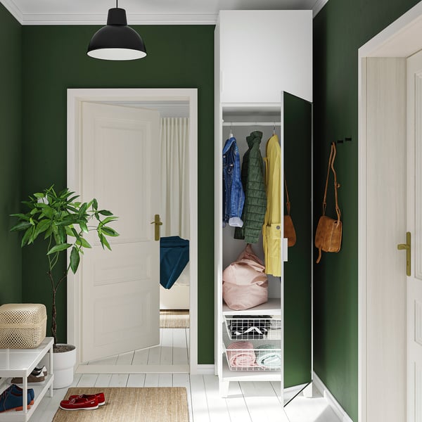 A modern entryway green walls, with a white PLATSA storage unit holding colourful coats and bags. A mirror door reflects light, enhancing the space.