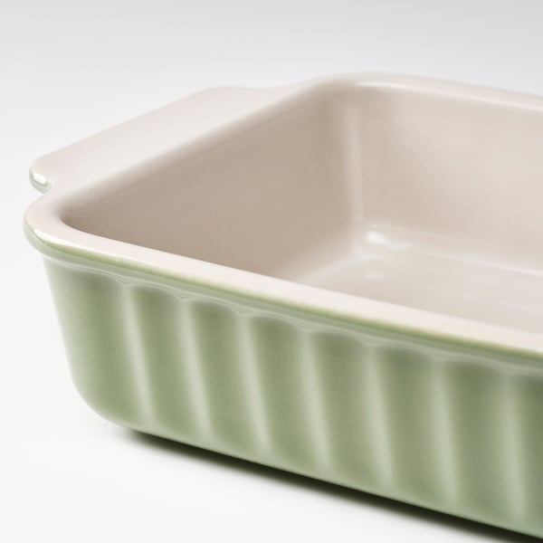 Oval baking dish with a ribbed, light green exterior and smooth, off-white interior. Handles for easy grip.