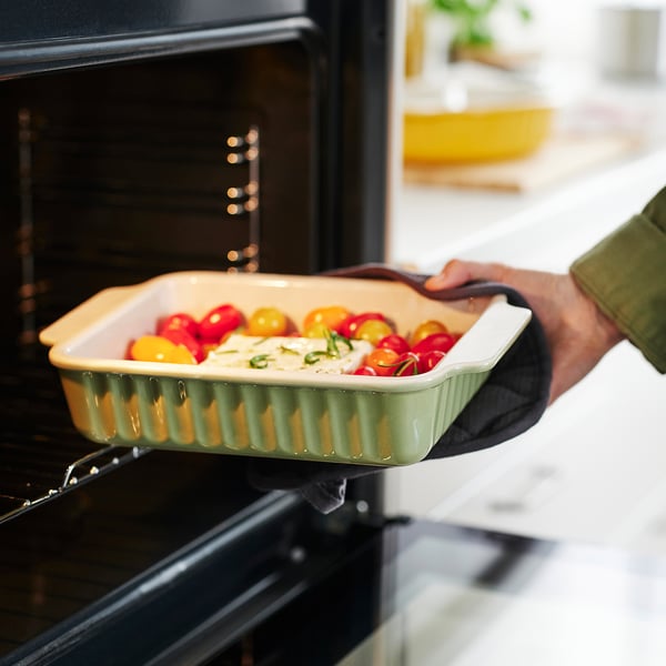 Person removes baked dish with tomatoes from oven.