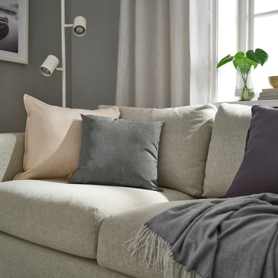 Modern living room with PROFETBLOMMA cushion on grey sofa near window with light grey curtains. Eco-friendly decor.