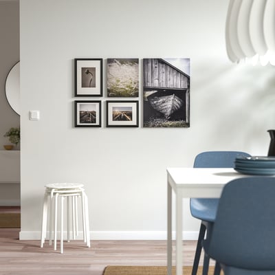 Black-and-white photos hang on wall, above stool and blue chairs.