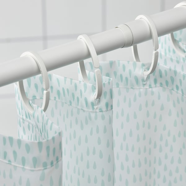 A white shower curtain with blue drop patterns hangs on plastic rings and rod, adding a fresh look to the bathroom.