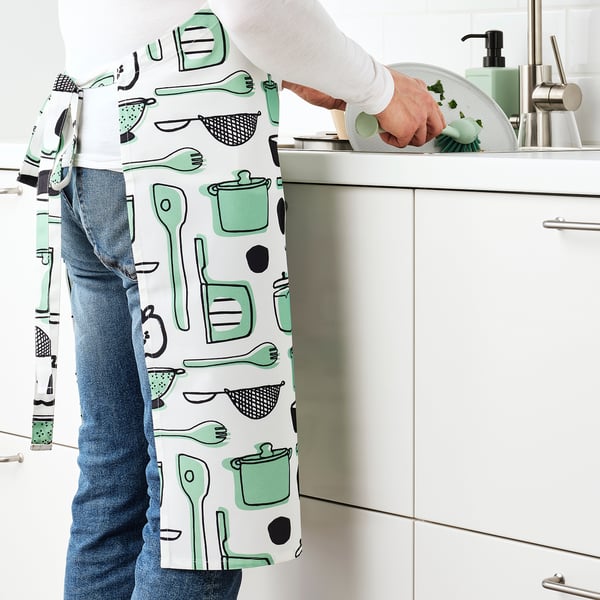 Person wearing a RINNIG apron, washing dishes in a modern kitchen with green and white apron repelling water.