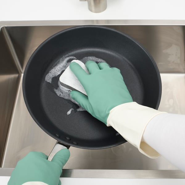 An a person wearing dish gloves cleaning a frying pan with a cloth.