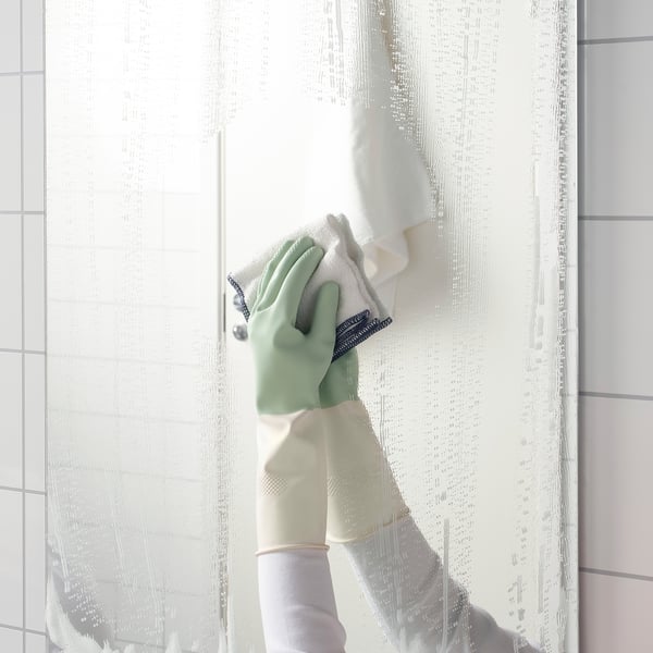 Person wearing green RINNIG dish gloves cleans a frosted glass door. Gloves help grip while cleaning.