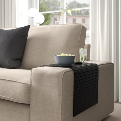 Sofa with beige upholstery and armrest tray holding bowl and drink. Tray folds, fits various armrest widths.