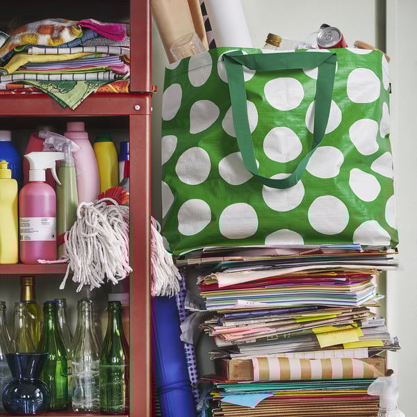 Green polka dot bag on cluttered shelf with cleaning supplies and documents.