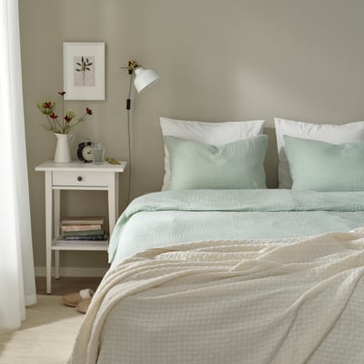 Bedroom with SCHERSMIN duvet, pillows, books, flowers, lamp, frame, and slippers.