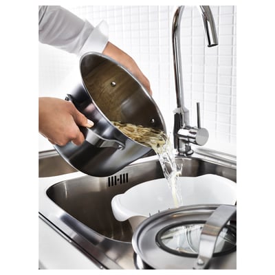 Person draining boiled noodles in a metal colander in a stainless steel sink.