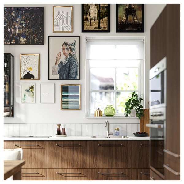 Modern kitchen with wooden cabinet, white counter, art gallery wall, and window sill decor.