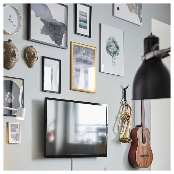 A wall a mirrored tv surrounded by various picture frames with abstract and natural themes, musical instruments, and decorative items.