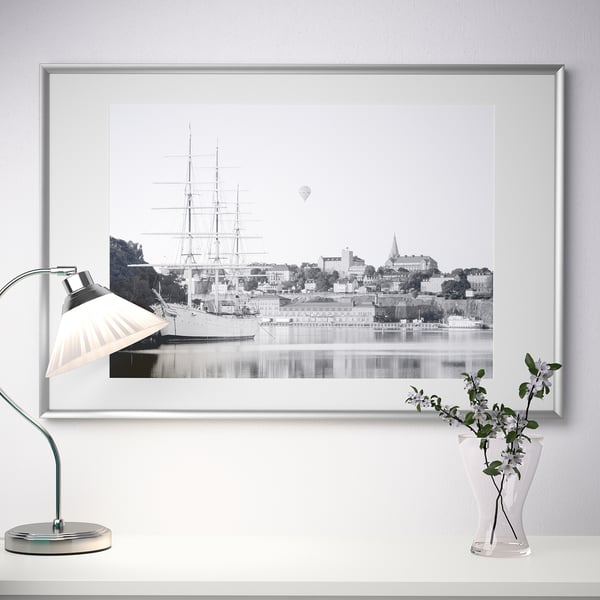 Framed maritime photo with desk lamp and vase. Wall art displayed on a table, showcasing a classic ship and cityscape.