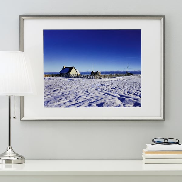 Framed snowy house on wall with lamp and books.