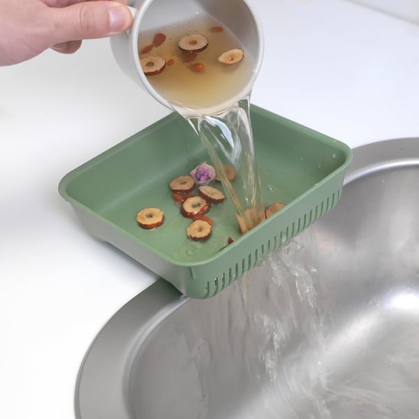 Pouring liquid into green strainer over sink; collects food waste, preventing drain blockages.