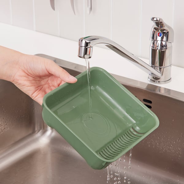 Hand fills green strainer under chrome kitchen tap, preventing drain clogs.