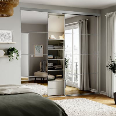 Modern bedroom with mirrored closet doors, green headboard bed, and large windows with grey curtains.