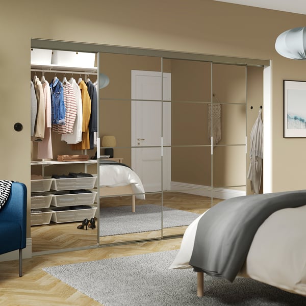 Bedroom with large mirrored SKYTTA wardrobe, reflecting bed and chair, complemented by blue chair.
