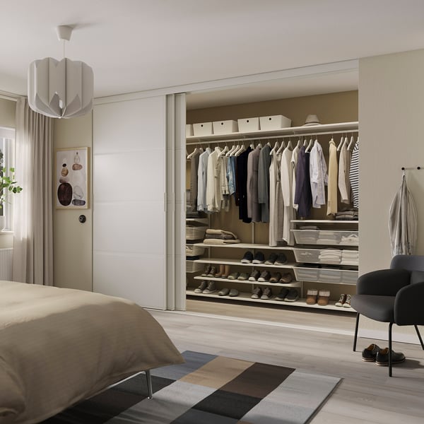 Modern bedroom with white closet, neat clothes, small bed, black chair, and patterned rug.
