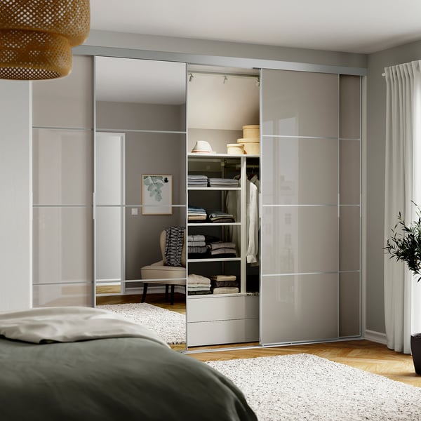 Modern bedroom with SKYTTA mirror closet, sleek reflective panels, dark green bed headboard, and open storage shelves.