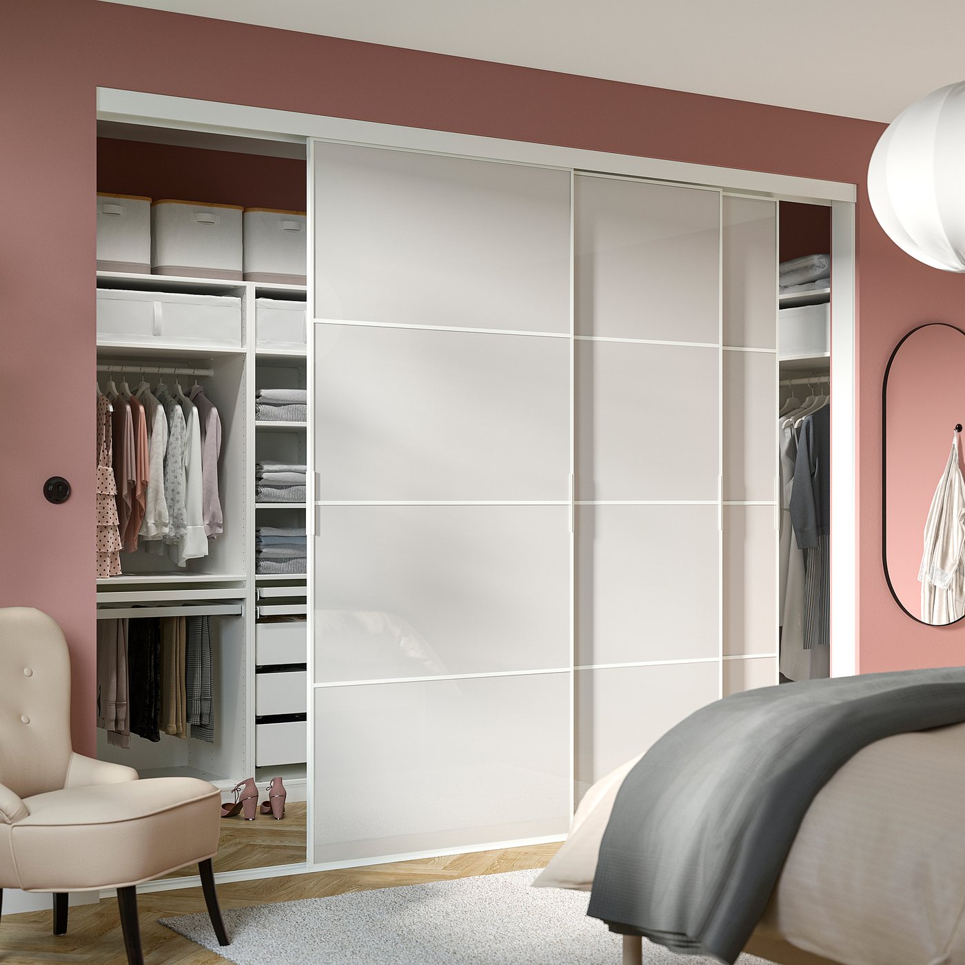 Modern bedroom with large SKYTTA wardrobe, white sliding doors, pink walls, organised clothes, beige chair, grey rug, bed, clock.