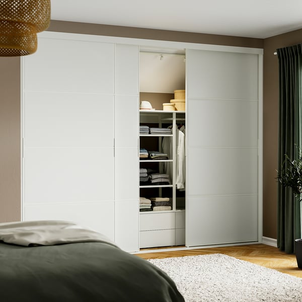 Modern bedroom with large white sliding wardrobe, containing neatly organised clothes and shelves, adjacent to a bed with green blanket.