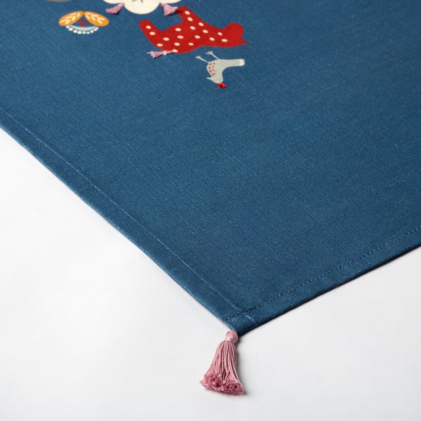 Hand-embroidered table runner on blue cotton, featuring colourful designs and tassel detail, showcasing quality craftsmanship.
