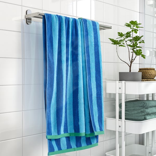 Blue & green striped towel on silver rail, near plant & folded towels.