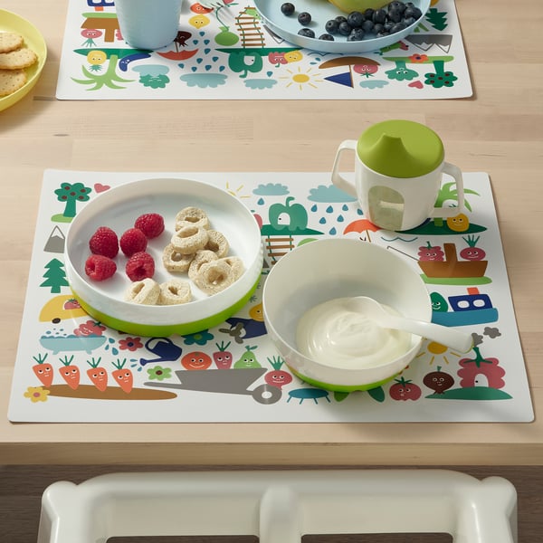 Childrens table setting with colourful placemat, plate, and bowl. The plate has inward-curving sides for easy scooping.