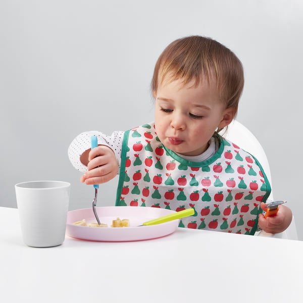 Child eating with colourful, grip-friendly cutlery, designed for learning to eat independently.