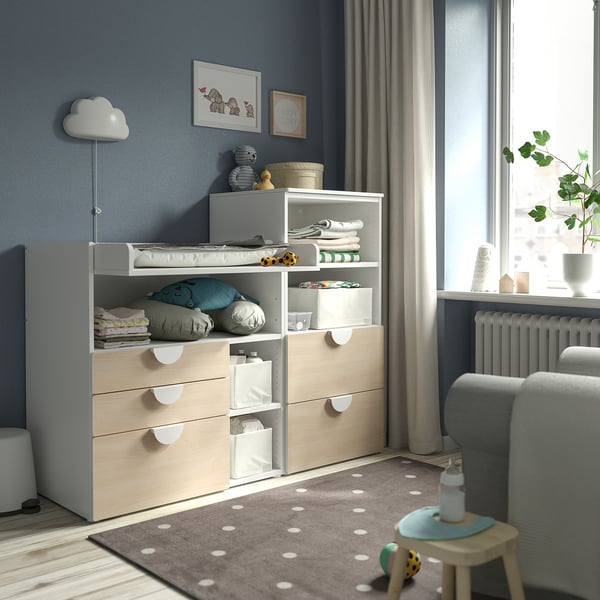 Modern nursery with changing table, storage, toys, rug, rocker, and natural light.