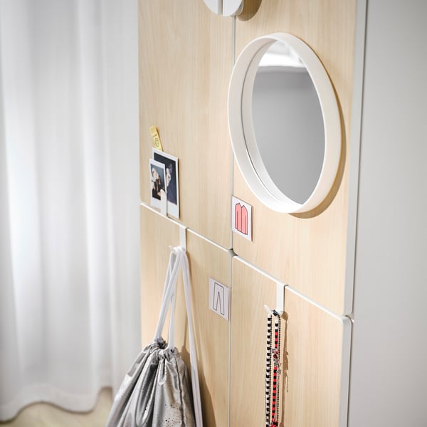 Light-colored wooden wardrobe with round mirror, photos, and hanging bags.