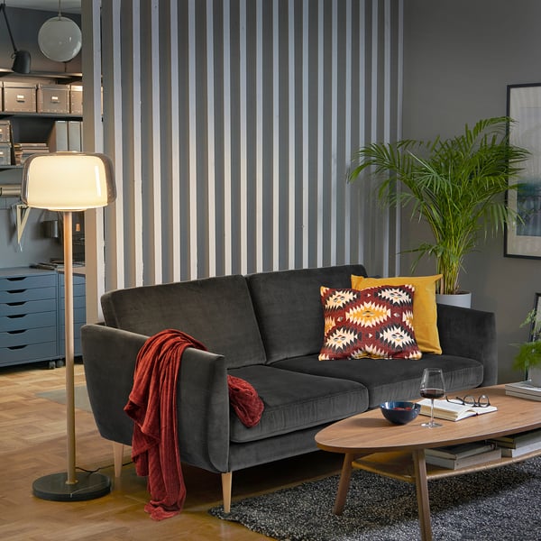 Modern living room with dark grey SMEDSTORP sofa, colourful pillows, wooden coffee table, floor lamp, and striped wallpaper.