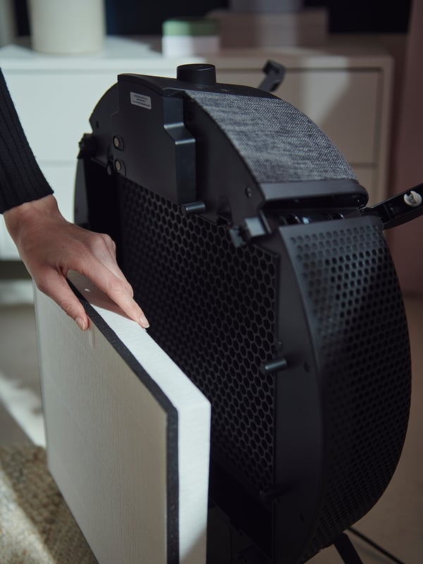 A person handles a black STARKVIND air purifier. Its front has honeycomb holes and a removable philtre.