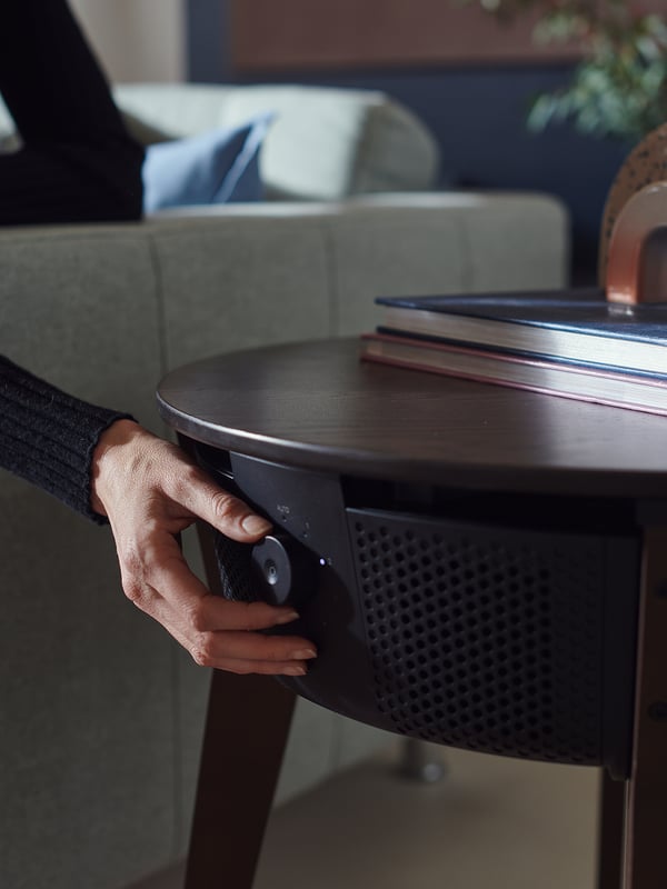 Image description: a hand adjusts a black ikea STARKVIND air purifier table in a cozy living room.
