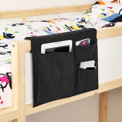 Black bed pocket on wooden bed frame. Holds tablet, phone, and book. Keeps items within reach for reading or other activities in bed.